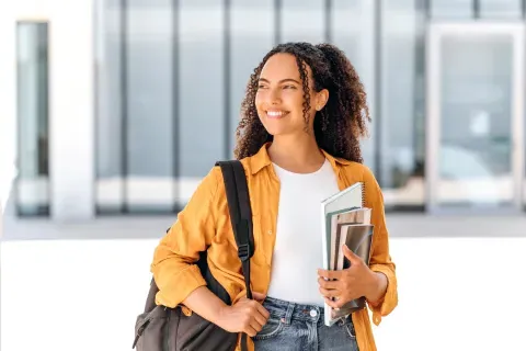 Student wearing backpack 和 smiling holding textbook